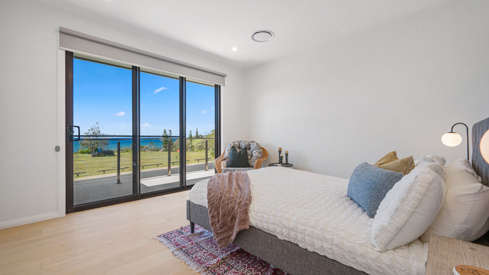 A bedroom with a large sliding glass door leading to a balcony with a view of the sea.