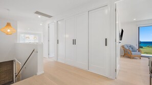 Un intérieur moderne avec un escalier, une grande armoire blanche et une vue sur la mer par une porte vitrée.