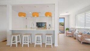 Une cuisine moderne avec des meubles blancs, un îlot central doté de tabourets et trois lampes suspendues.