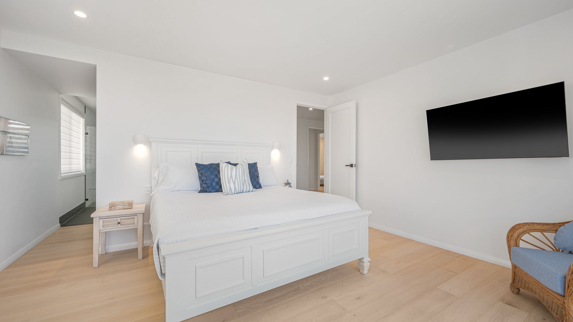 Une chambre à coucher avec un grand lit, une table de chevet, une chaise, un téléviseur à écran plat et une porte donnant sur une autre pièce.