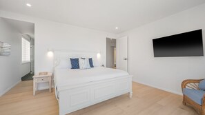Une chambre à coucher avec un grand lit, une table de chevet, une chaise, un téléviseur à écran plat et une porte donnant sur une autre pièce.