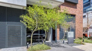 A modern building with a glass entrance, a tree in front, and a parking sign. - 360 Essential Brooklin (São Paulo)