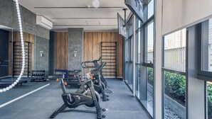 A modern gym with exercise equipment, large windows, and a view of the city. - 360 Essential Brooklin (São Paulo)