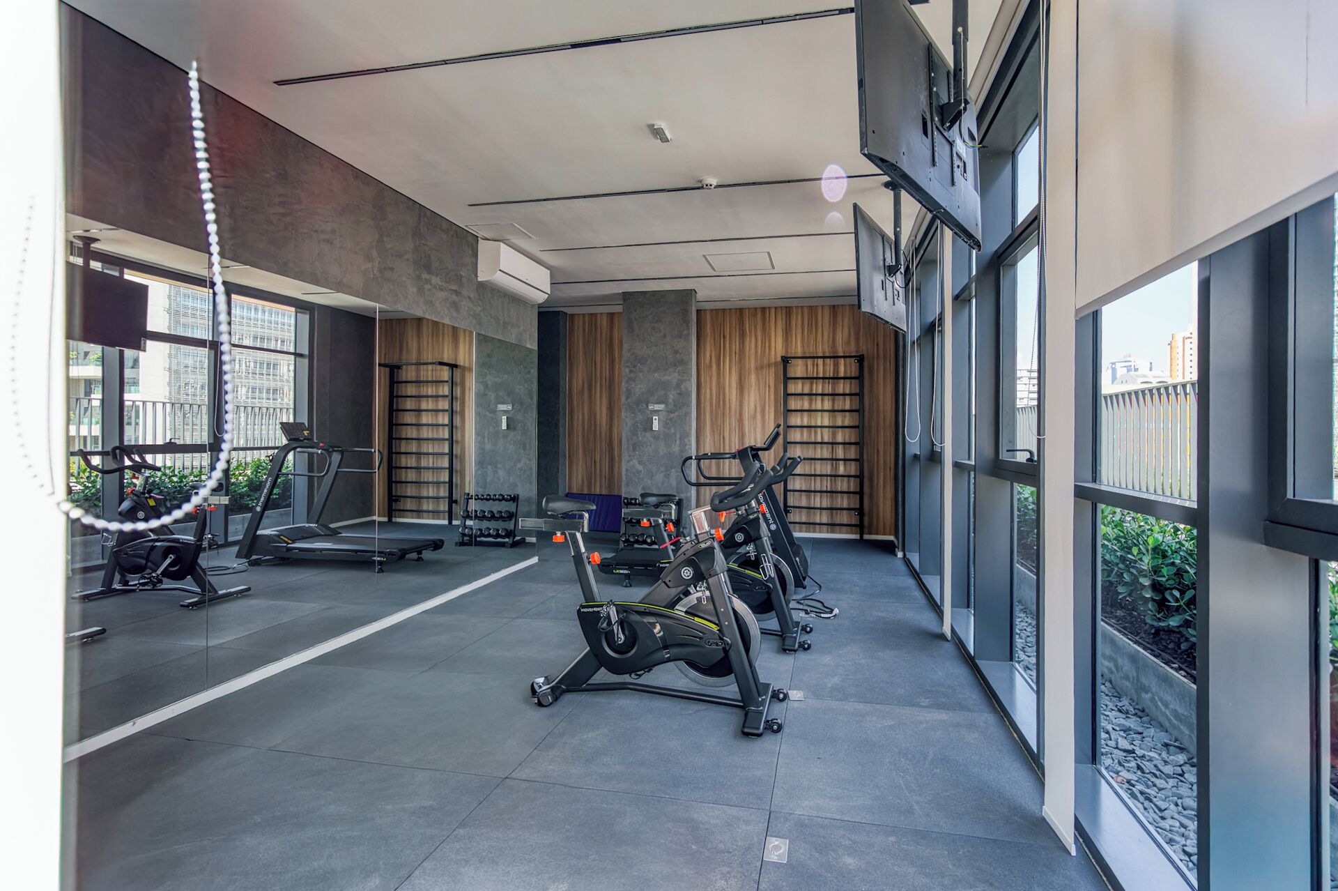 Une salle de sport moderne équipée de machines de cardio, d’appareils de musculation et dotée d’une grande fenêtre laissant entrer la lumière naturelle.