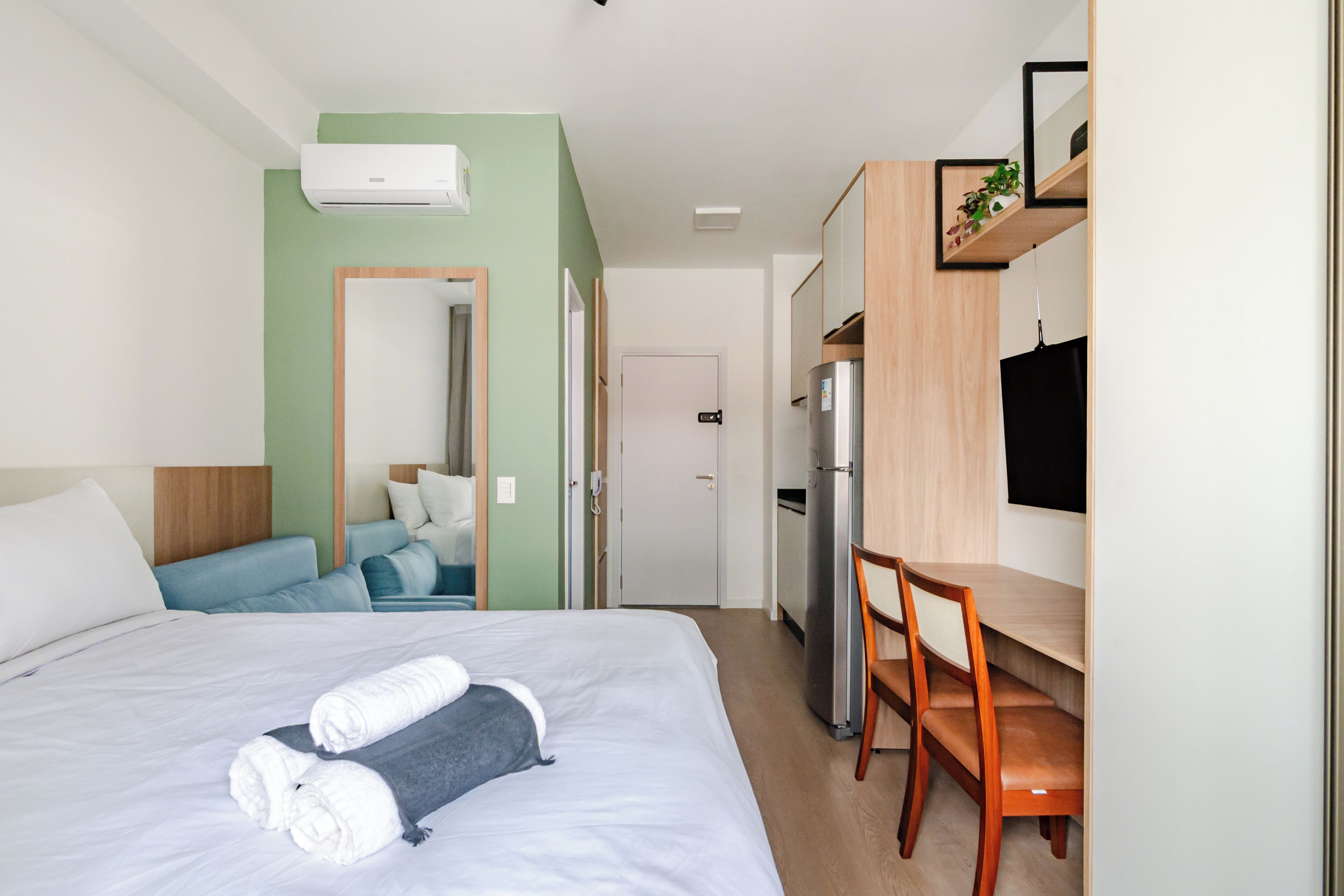 Quarto de hotel com cama, escrivaninha, frigorífico e televisão.