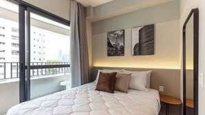 A hotel room with a large bed, a small table, and a view of buildings through a balcony. - 360 Essential Brooklin (São Paulo)