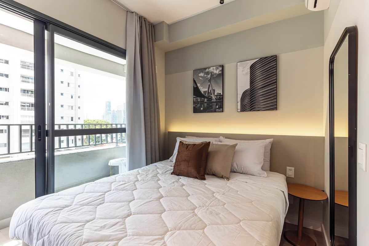 A hotel room with a large bed, a small table, and a view of buildings through a balcony.