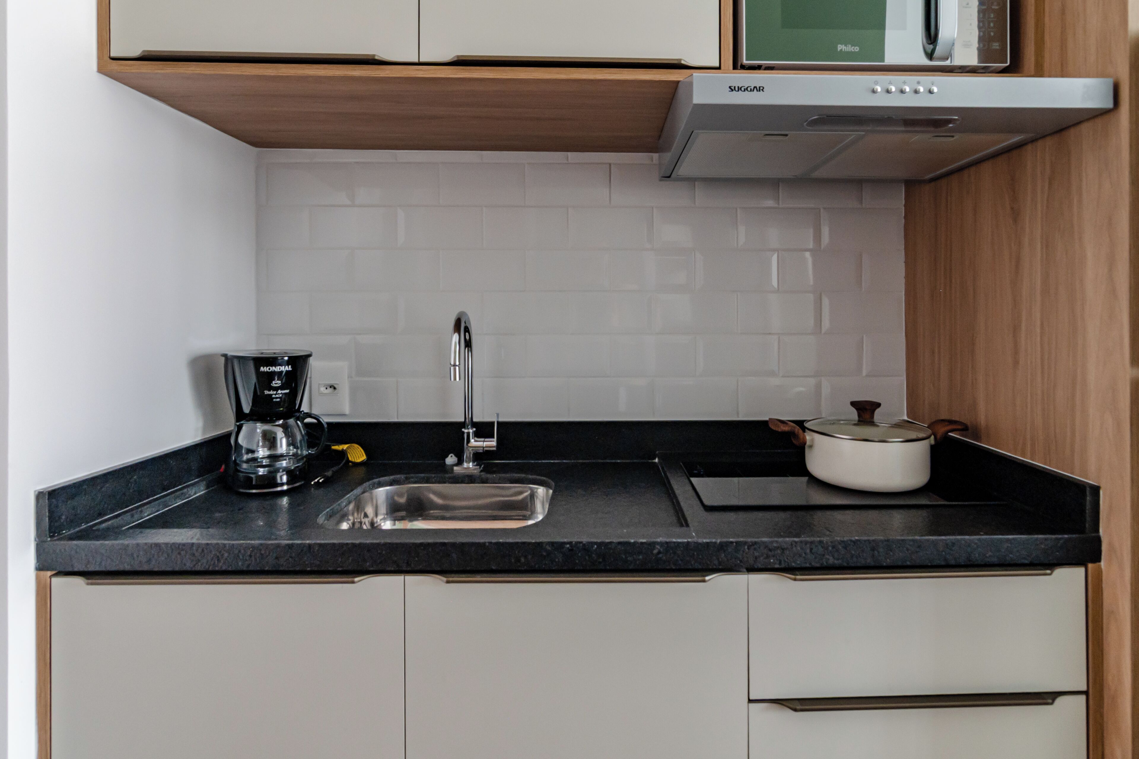 Una cocina compacta con encimera negra, pileta de acero inoxidable, cafetera y microondas.