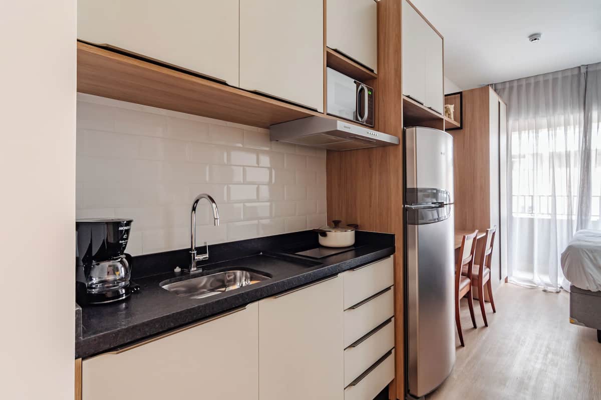A modern kitchen with a built-in microwave, coffee maker, and stainless steel refrigerator. There is a dining area with a table and chairs visible through a large window.