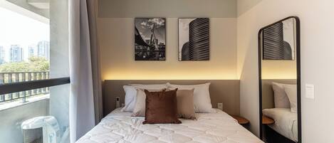 A hotel room with a large bed, a balcony, and two artworks on the wall.