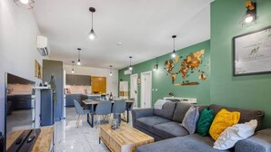 A modern living room with a grey sofa, a wooden coffee table, and a dining area with a table and chairs. There is a kitchen visible in the background. - The Green Haven in the Heart of St Julians (Saint Julian's)