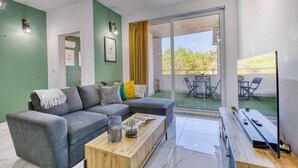 A modern living room with a grey sofa, a wooden coffee table, and a glass door leading to a balcony with outdoor seating. - The Green Haven in the Heart of St Julians (Saint Julian's)
