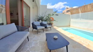 Un espace aménagé au bord de la piscine, avec un sol en pierre, une table bleue, deux canapés gris et une plante en pot.