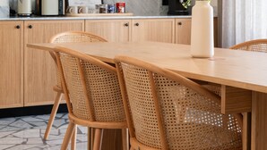 Une cuisine moderne avec un pare-feu en marbre, des armoires en bois et un coin repas comprenant une table en bois et des chaises en rotin.