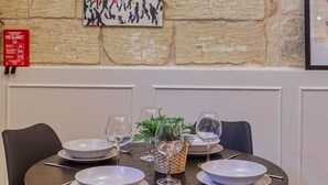 Zona pranzo con parete in pietra, un rilevatore di fumo e un tavolo imbandito per quattro persone con sedie.