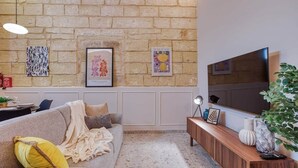 Un soggiorno con parete in pietra, un divano, un tavolino da caffè, una TV e opere d'arte incorniciate.