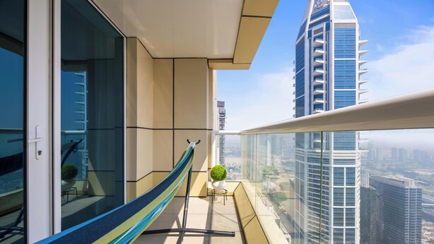 A balcony with a hammock, a small table with a plant, and a view of tall buildings.