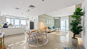 A modern kitchen with a dining area, a living room with a sofa and a coffee table, and a large potted plant.