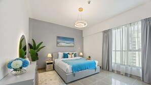 A modern bedroom with a large bed, a bedside table, a nightstand, a mirror, a potted plant, and a window with curtains.