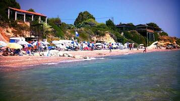 A beach with umbrellas and people, a building with a red roof, and a clear sky.
