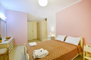 Una camera da letto con un letto, comodini, uno specchio, una cassettiera e una porta che dà su un'altra stanza.