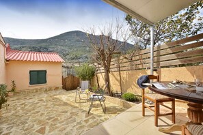A patio with stone flooring, a table with chairs, a wooden fence, and a view of a mountain.