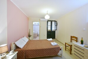 A bedroom with a bed, bedside table, lamp, and a desk with a bottle.
