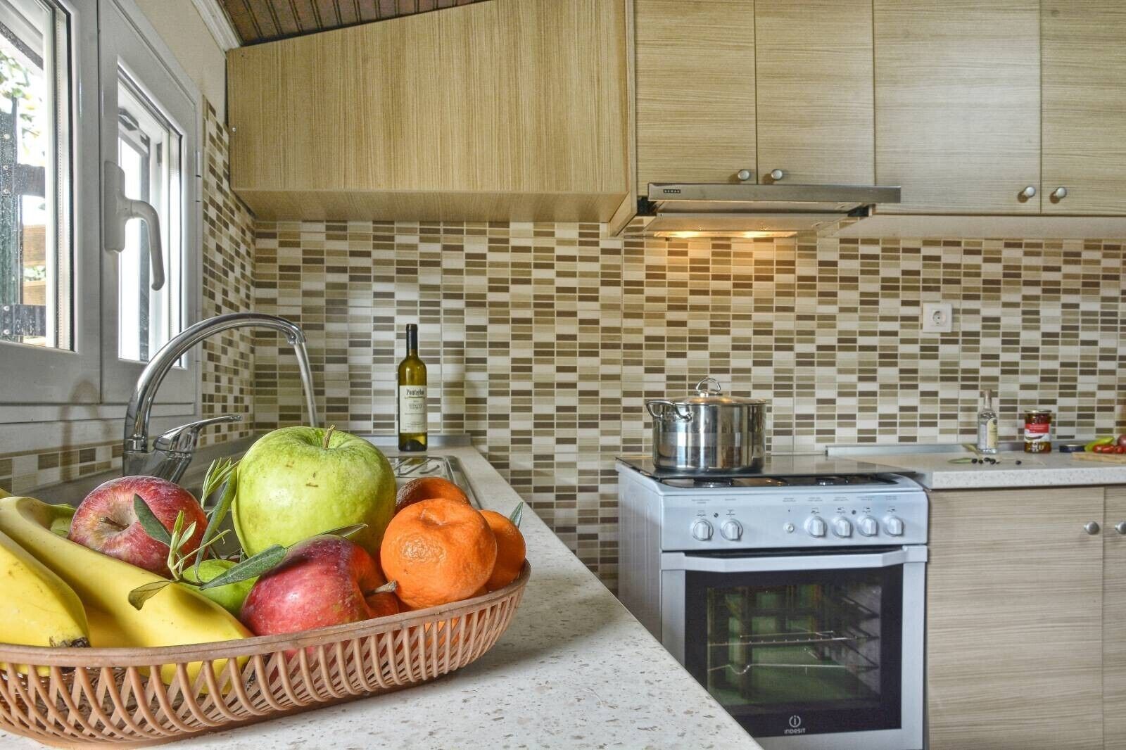 A kitchen with a tiled backsplash, a stove, a sink, and a fruit basket.