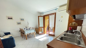 Un espacio habitable compacto con comedor, kitchenette y puerta corrediza de vidrio que da a un área exterior.