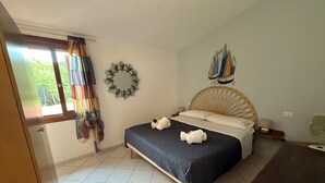 Un dormitorio con cama, ventana con cortinas, un adorno en la pared y una mesita de noche pequeña.