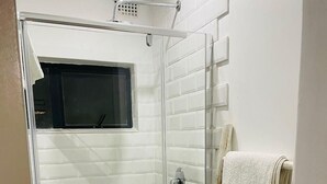 Une douche fermée par des parois en verre, un sol carrelé, un porte-serviettes avec plusieurs serviettes et une fenêtre située au-dessus de la douche.