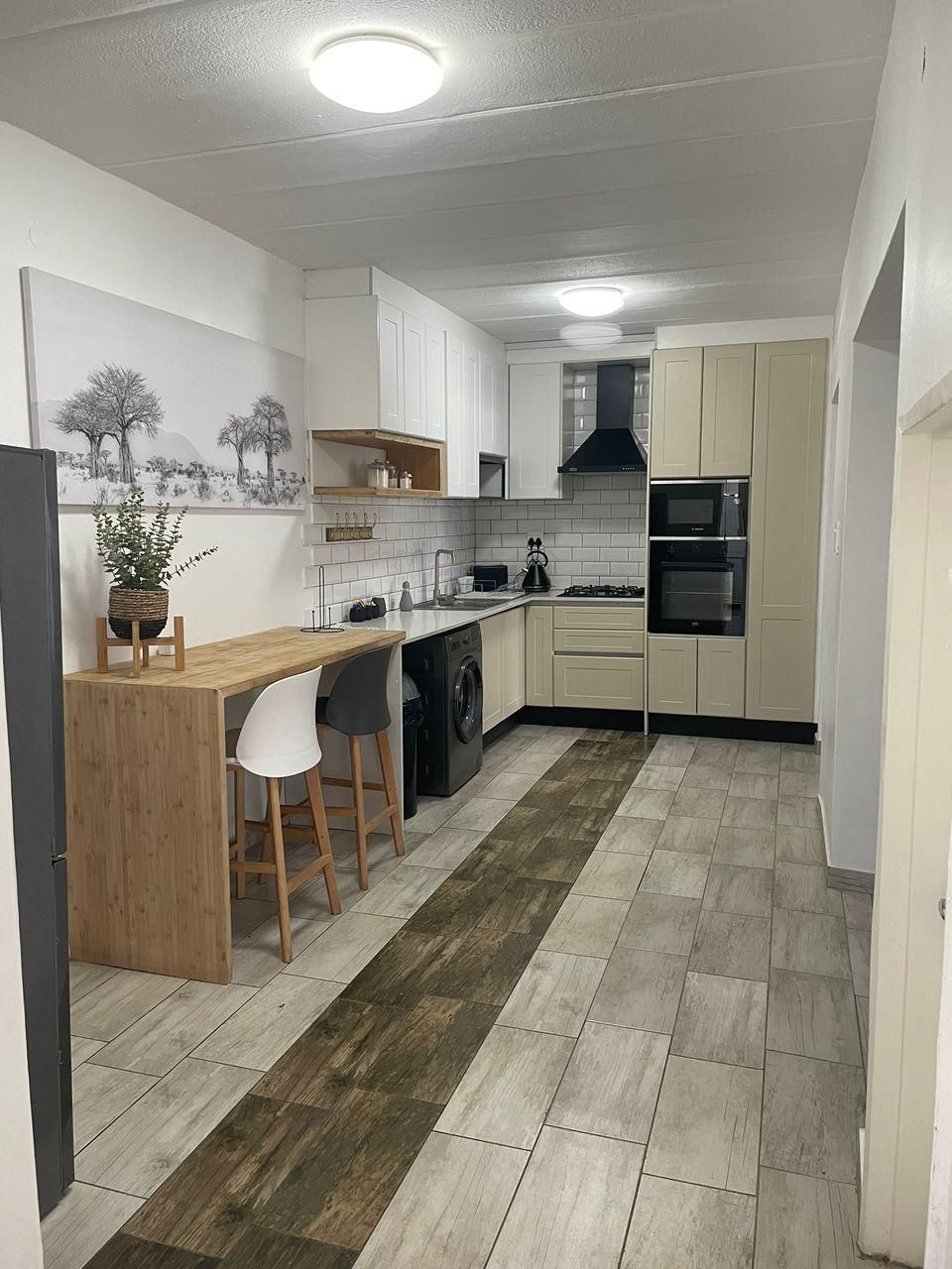 A modern kitchen with white cabinets, a wooden bar counter, a washing machine, and a dining area with a chair.