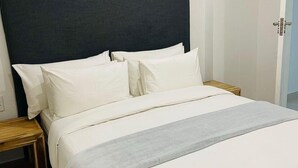 Un lit bien fait, avec une tête de lit sombre, une literie blanche et un plaid gris.