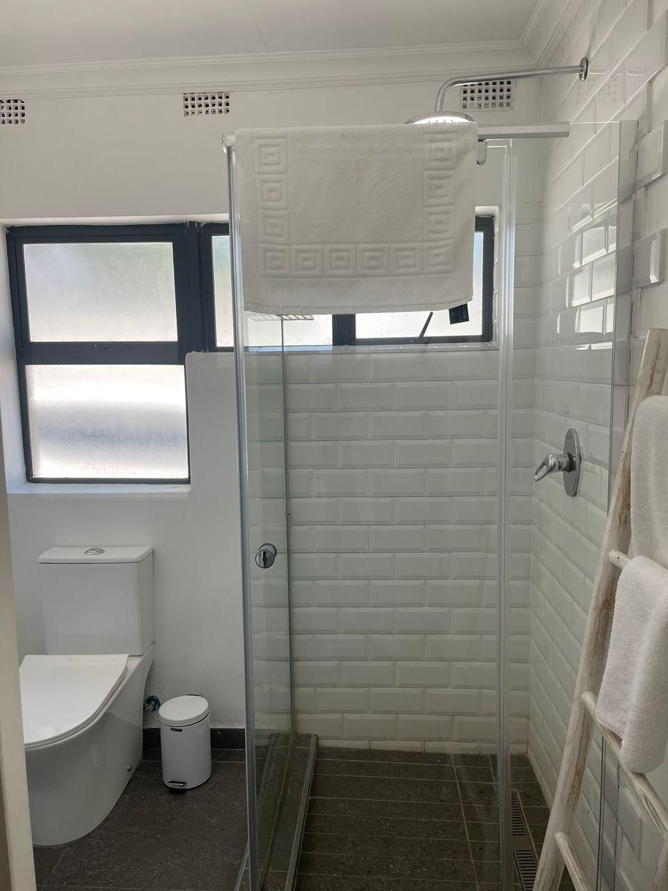 A small, white bathroom with a toilet, a trash can, and a shower area with a glass door.