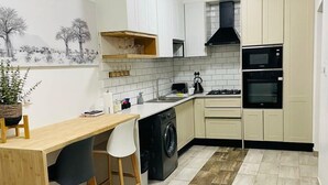 Une cuisine compacte avec des meubles blancs, une table à manger en bois, un lave-linge et un four à micro-ondes.