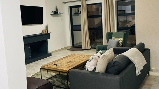 Un salon moderne avec un canapé gris, une table basse en bois, un téléviseur à écran plat et une cheminée.