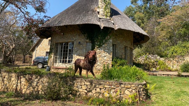 A stone house with a thatched roof and a lion statue in front. - Beautiful Round Shaped Cottage - 2094 (Juliasdale)