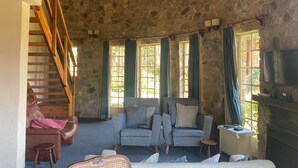 A cozy living room with a stone ceiling, a wooden staircase, a sofa, a television, and a fireplace. - Beautiful Round Shaped Cottage - 2094 (Juliasdale)