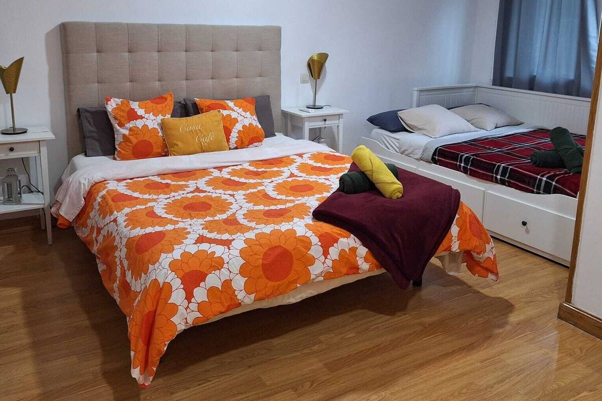 A bedroom with two beds, a nightstand, an air conditioning unit, and a window with curtains.