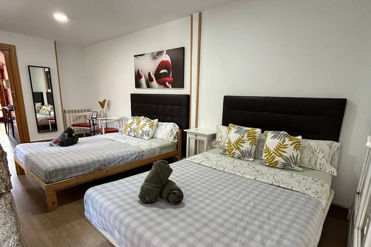 A hotel room with two beds, a mirror, a painting, and a small table.