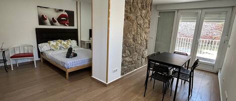 Una stanza con un letto, un tavolo da pranzo con sedie, una sedia bianca e un muro in pietra.