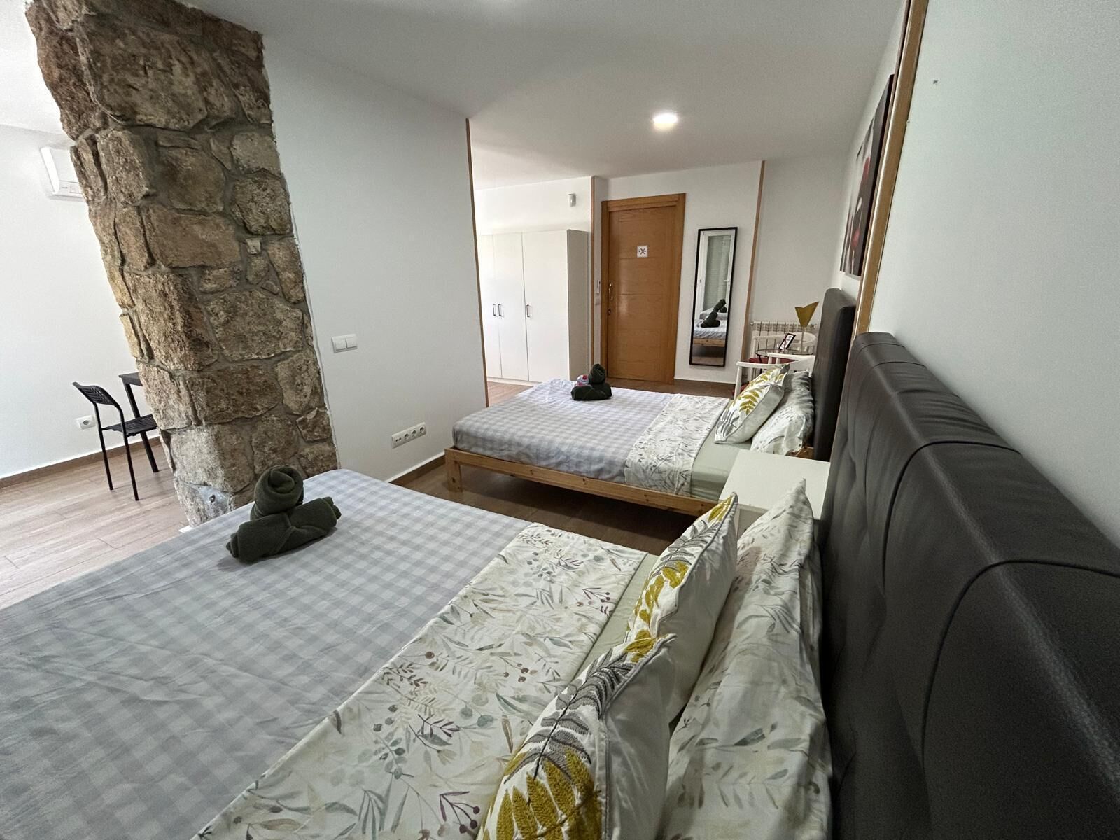 Une chambre avec deux lits, un mur en pierre, un plancher en bois, un canapé et une petite table avec une chaise.