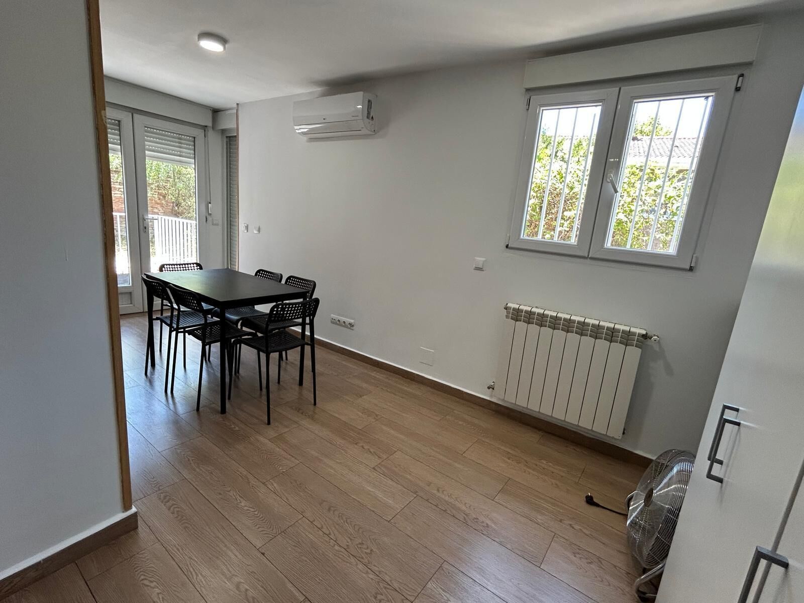 Una habitación con una mesa de comedor y sillas, una ventana con persianas, un radiador y un equipo de aire acondicionado.