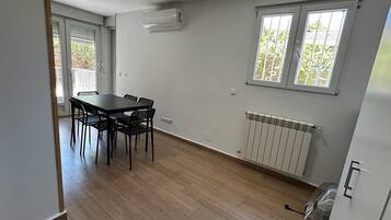Una habitación con una mesa de comedor y sillas, una ventana con persianas, un radiador y un equipo de aire acondicionado.