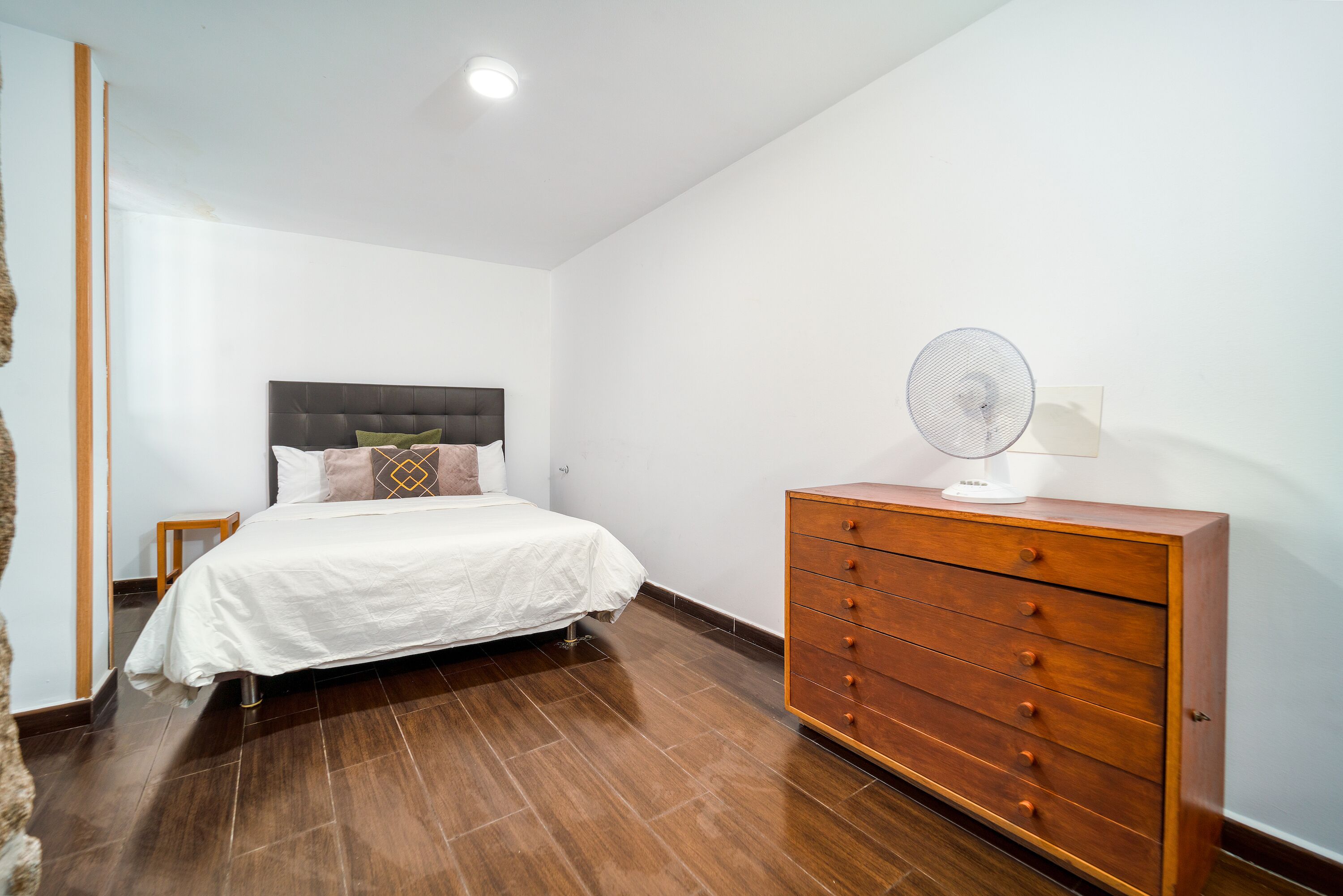 Une chambre à coucher avec un lit, une commode en bois et un ventilateur de plafond.