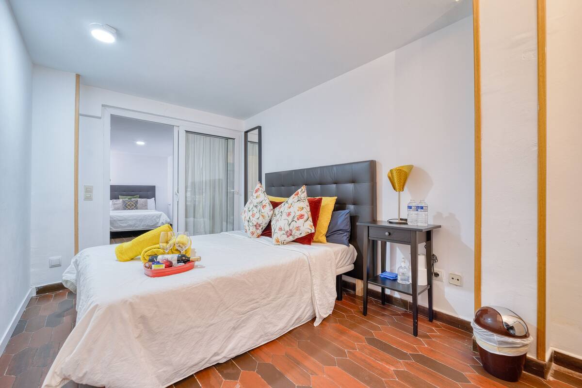 A hotel room with a large bed, a bedside table with a lamp, and a trash bin.