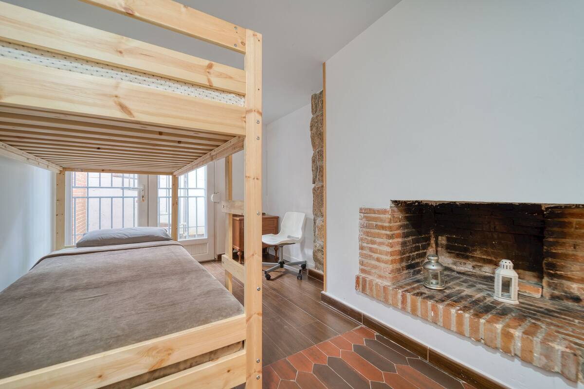 A room with a bunk bed, a brick fireplace, and a desk with a chair.
