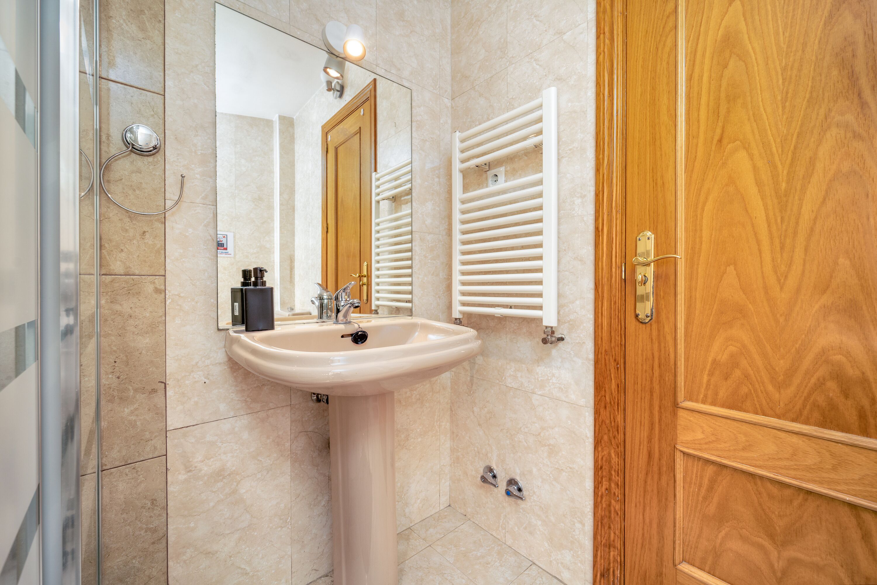 Un baño con lavamanos, espejo, toallero y puerta de madera.