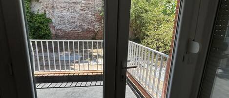 Vista desde una ventana a un balcón con pared de ladrillo y vegetación.