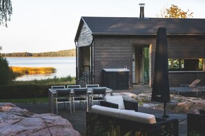 A wooden cabin with a deck, outdoor seating, and a view of a lake.